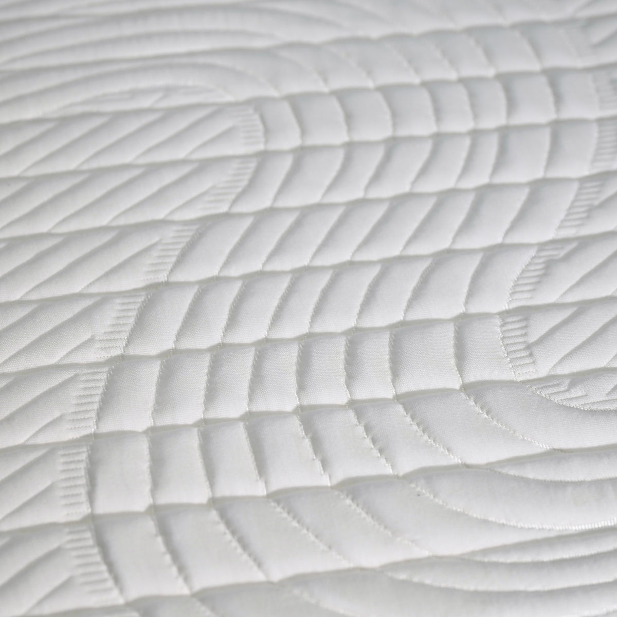 Gros plan sur la surface matelassée du matelas OLCODREAM, tissu blanc au motif ondulé